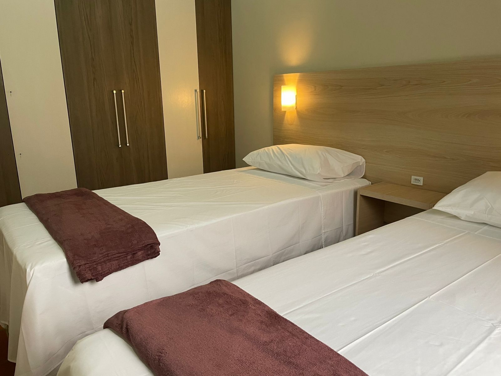 A hotel room with two single beds, a wooden headboard, a nightstand, and a wardrobe with two doors.