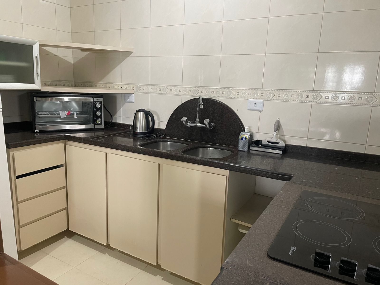 A compact kitchen with a microwave, kettle, sink, and stove.