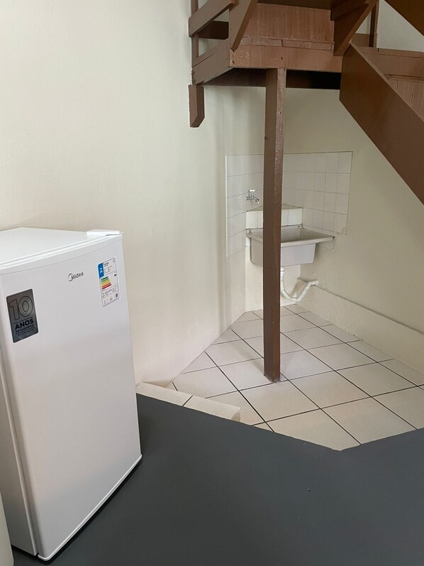 A compact kitchen with a white refrigerator, a small sink, and a wooden staircase. - Pousada Recanto Do Costão (Florianópolis)