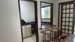 A compact kitchen with white tiles, a black countertop, and a window. There are two wooden chairs and a glass-top table. - Pousada Recanto Do Costão (Florianópolis)