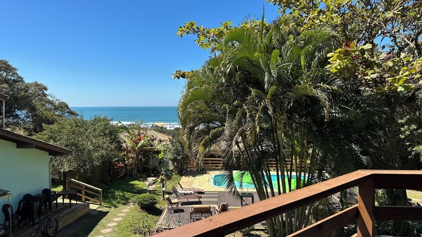 A view of a pool area with a wooden deck, lounge chairs, and a clear blue sky. - Pousada Recanto Do Costão (Florianópolis)