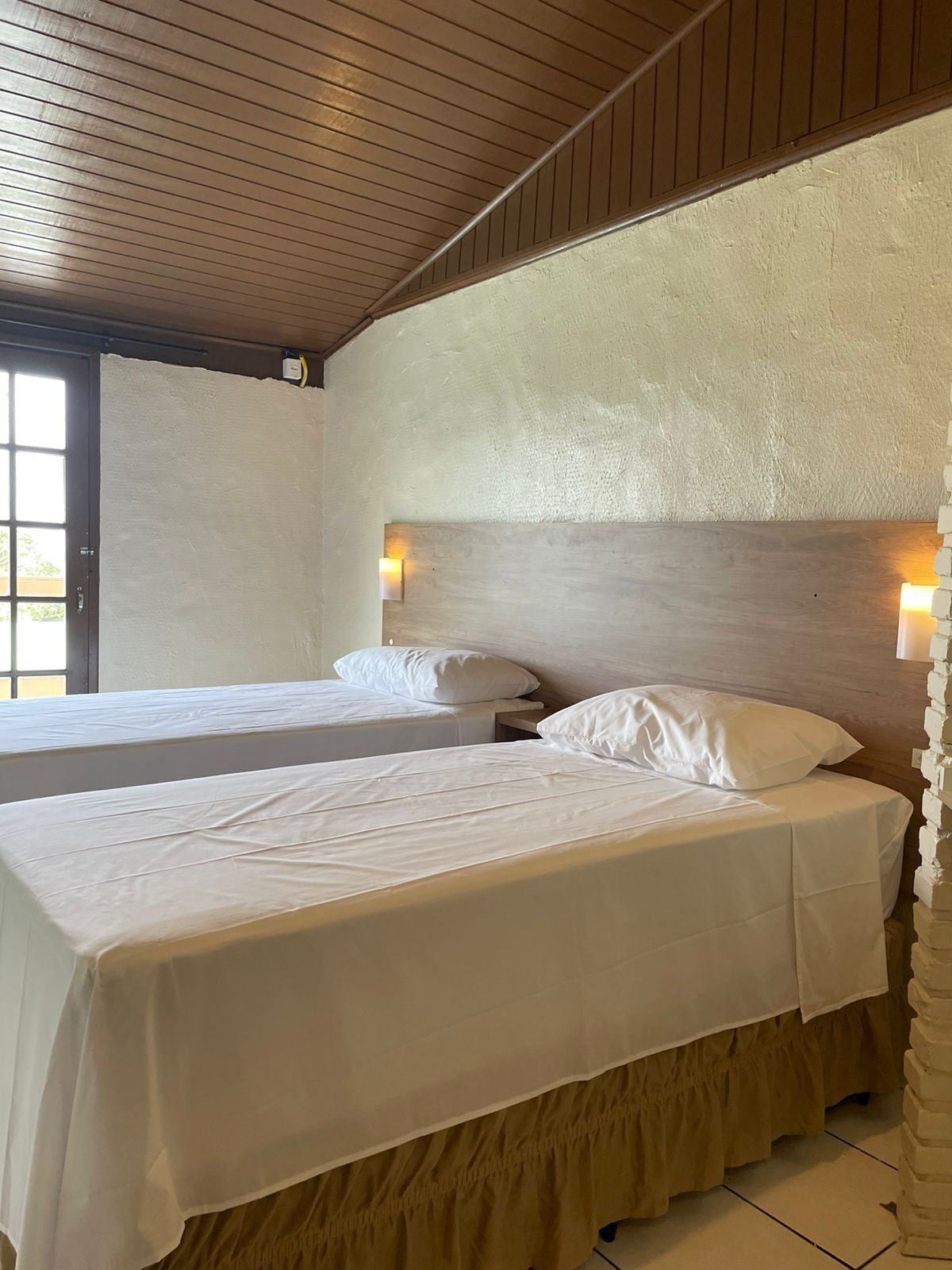 A room with two beds, wooden ceiling, and a textured wall.