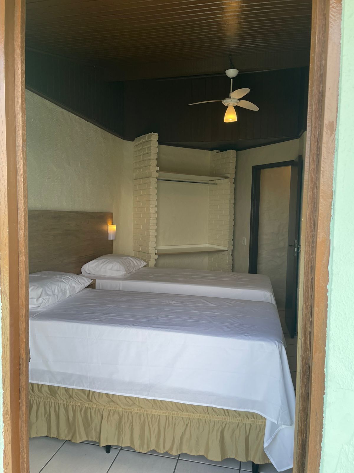 A room with two beds, a ceiling fan, and a wall-mounted light.