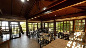 A spacious indoor area with wooden tables and chairs, large windows, and a ceiling fan. - Pousada Recanto Do Costão (Florianópolis)