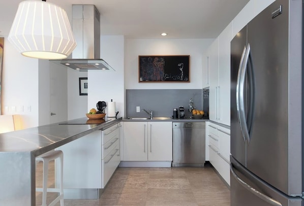 A modern kitchen with a stainless steel refrigerator, a built-in dishwasher, and a pendant light above the island.