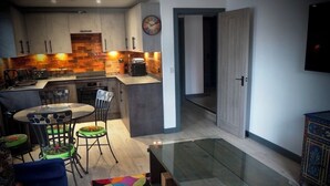 Eine moderne Küche mit Ziegelrückwand, einem Essbereich mit Glastisch und einem farbenfrohen Teppich.