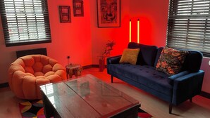 Ein modernes Wohnzimmer mit einem blauen Sofa, einem orangefarbenen Sessel und einem Glastisch.