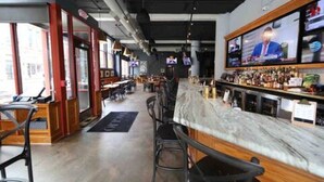 A bar area with a marble countertop and multiple screens displaying news. - OTR by TQL+Studio+Queen Bed+50inTV+4th Fl+Sleeps 3ppl (Cincinnati)