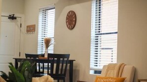 A cozy living room with a sofa, a coffee table, and a chair. There is a clock on the wall and a window with blinds. - OTR by TQL+Studio+Queen Bed+50inTV+4th Fl+Sleeps 3ppl (Cincinnati)