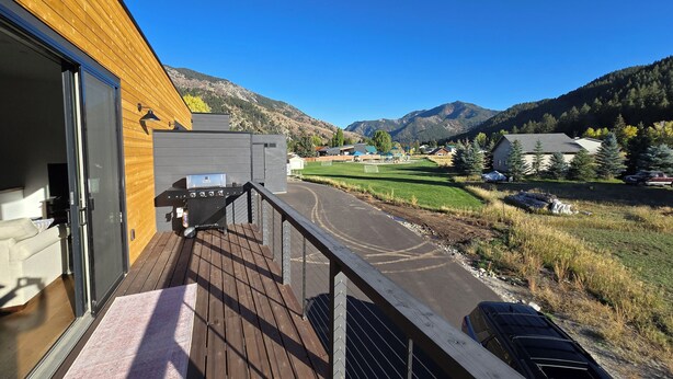 Um terraço com churrasqueira, um edifício de madeira e vista para um campo verde e montanhas.