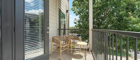 A balcony with a sliding glass door, two wicker chairs, and a small round table.