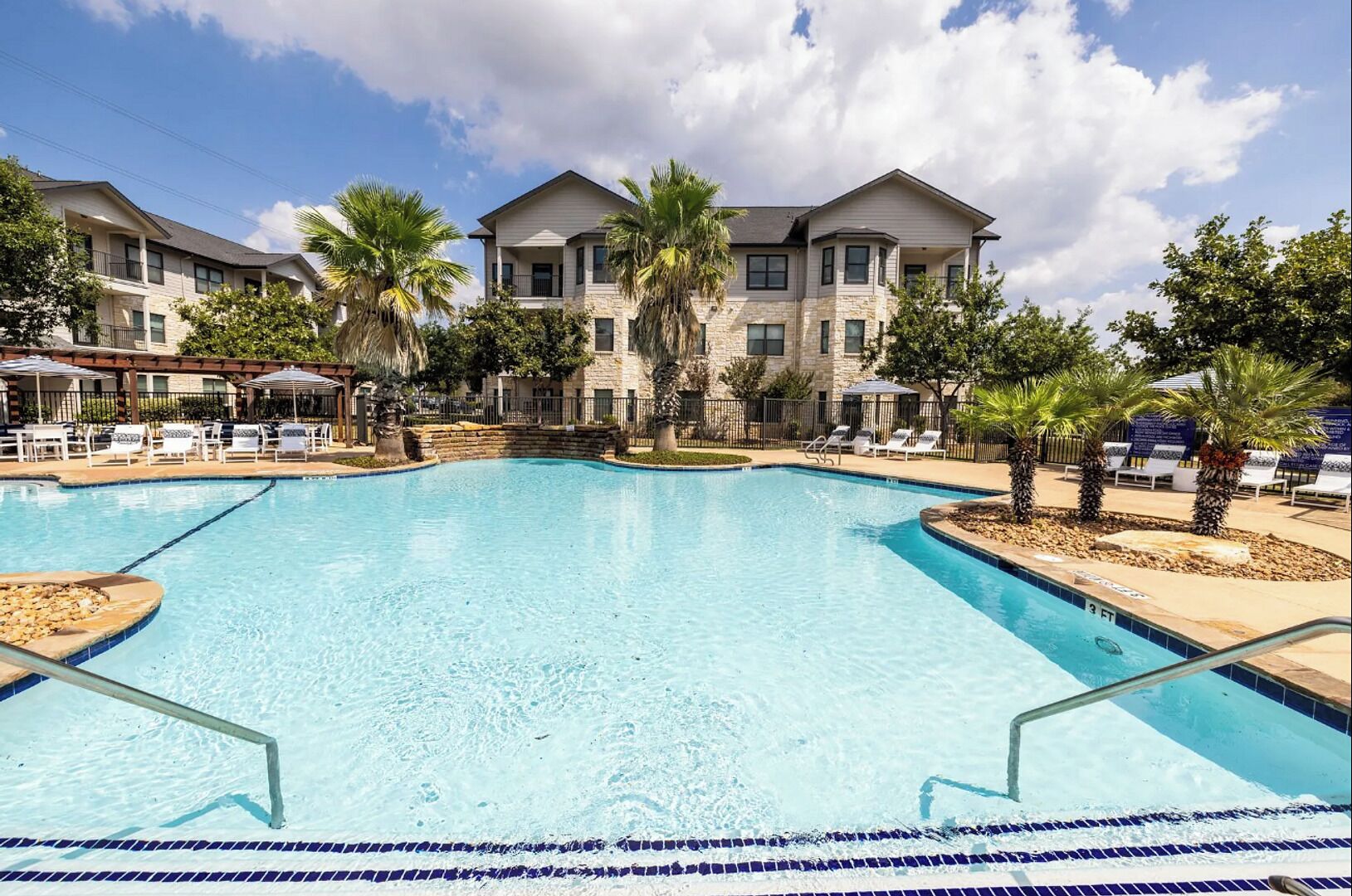 A swimming pool with a clear blue water, surrounded by lounge chairs and palm trees.