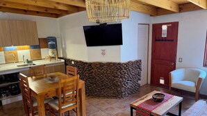 A cozy kitchen with a dining area, a stone wall, and a television mounted on the wall. - Tambo Atacama Lodge (San Pedro de Atacama)