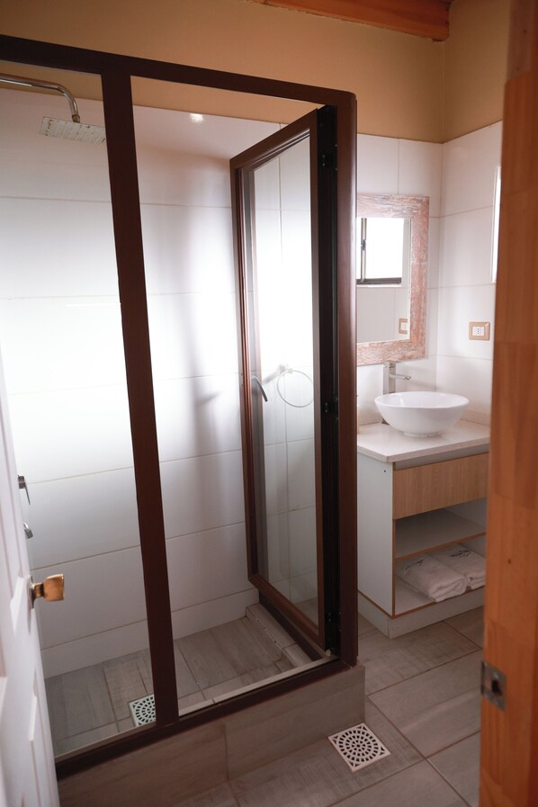 A modern bathroom with a glass-enclosed shower, a white sink, and a wooden vanity. - Tambo Atacama Lodge (San Pedro de Atacama)
