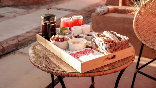 A wicker table with a tray of food and drinks, a wicker chair, and a building in the background. - Tambo Atacama Lodge (San Pedro de Atacama)