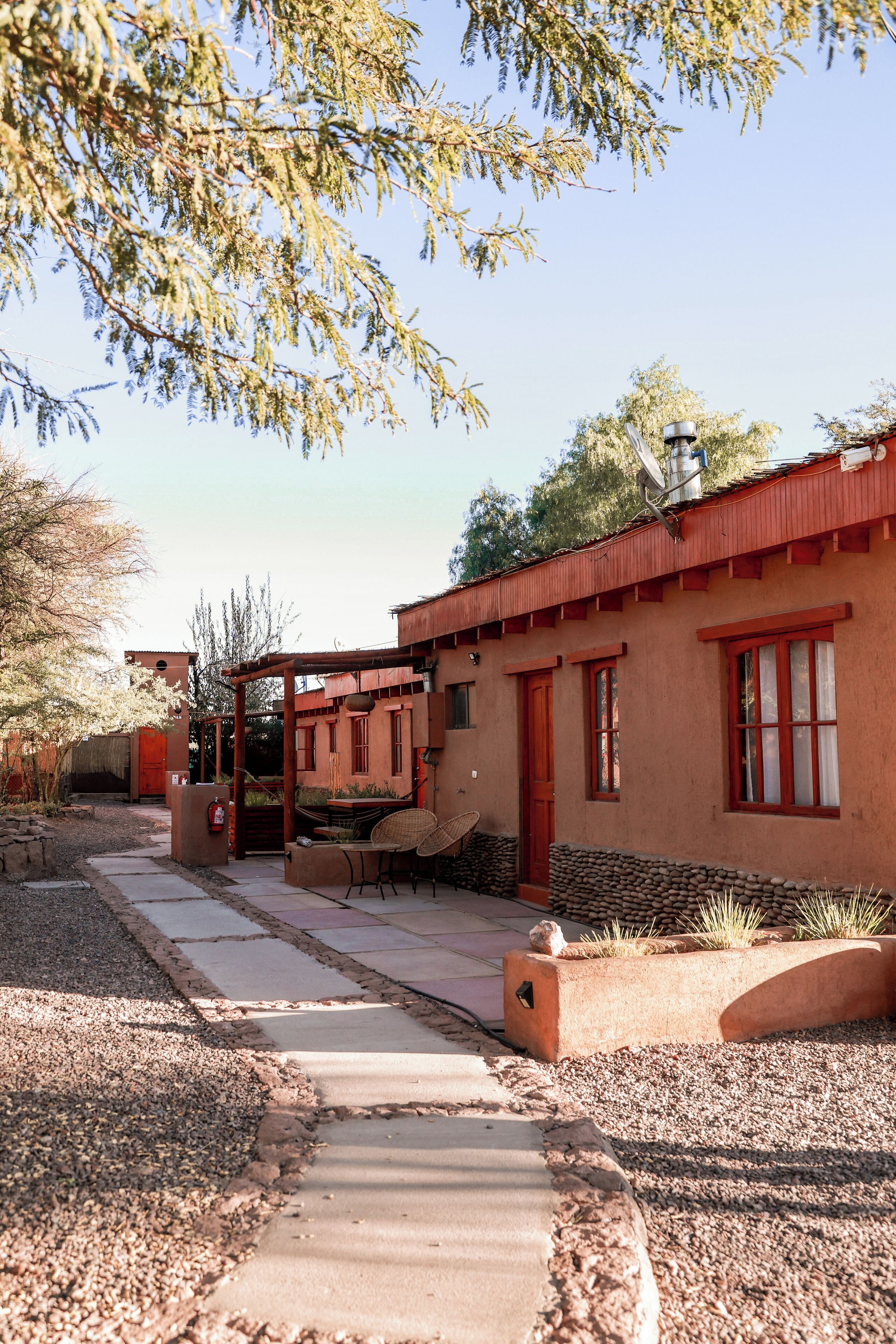 A rustic building with a red roof, a covered patio, and a gravel pathway leading to the entrance.