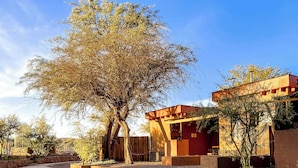 A courtyard with a stone fire pit, a tree, and a building with a red roof. - Tambo Atacama Lodge (San Pedro de Atacama)