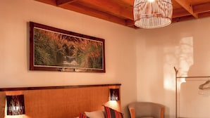 A bedroom with a wooden headboard, a large bed with striped bedding, a hanging light fixture, and a painting on the wall. - Tambo Atacama Lodge (San Pedro de Atacama)