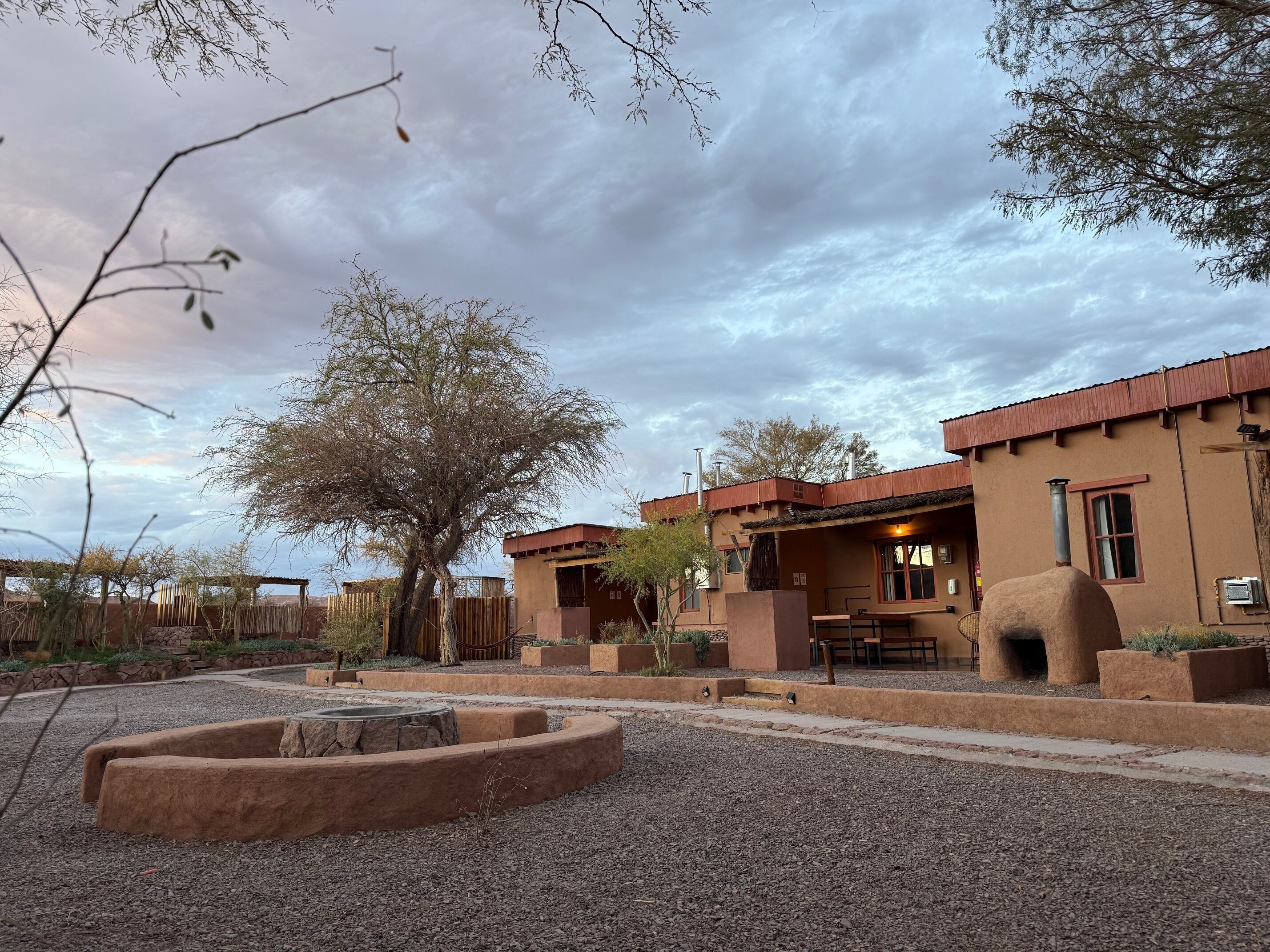Un bâtiment rustique doté d’un patio, d’un foyer et d’un grand arbre en premier plan.