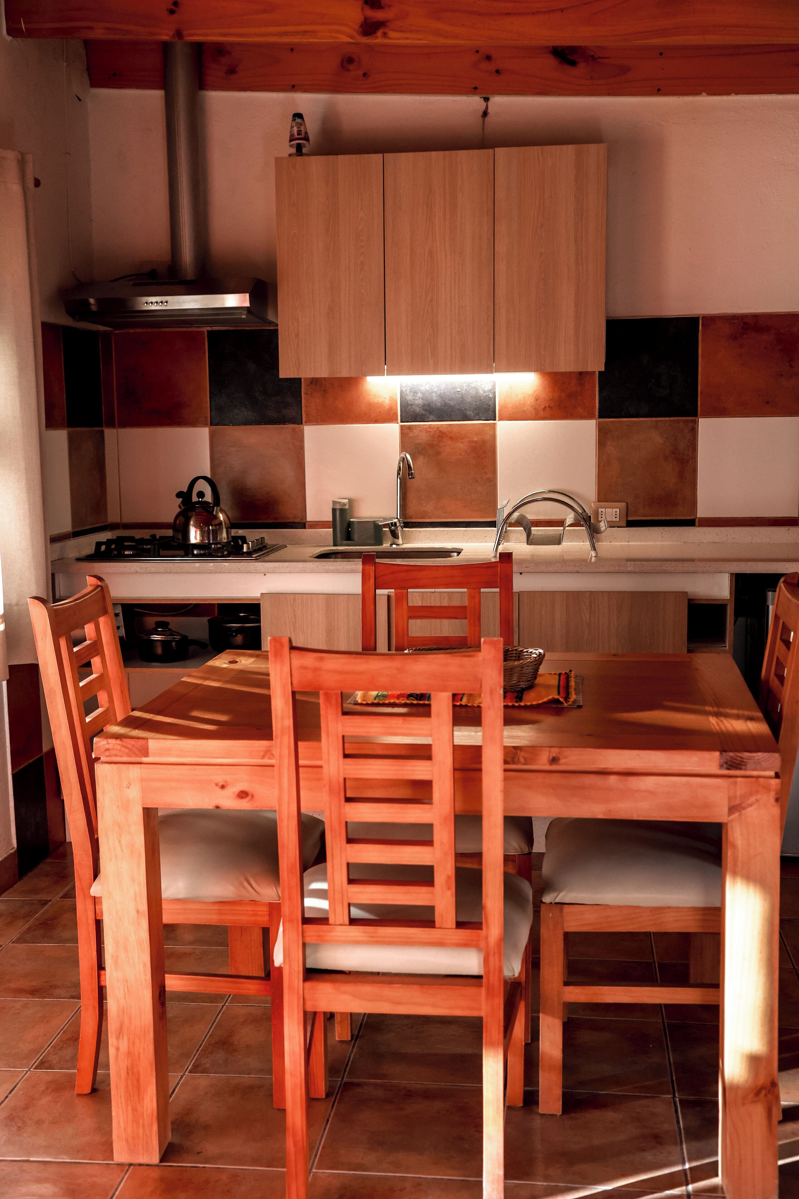 A wooden dining table with four chairs, a kitchen with a stove and sink, and wooden cabinets.