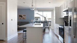 A modern kitchen with a central island, stainless steel appliances, and a dining area with a view to the outside. - Landing | Stylish 1BD, Clubhouse, Gym (Oakwood)