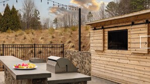An outdoor patio with a grill, a stone wall, and a wooden building with a window. - Landing | Stylish 1BD, Clubhouse, Gym (Oakwood)