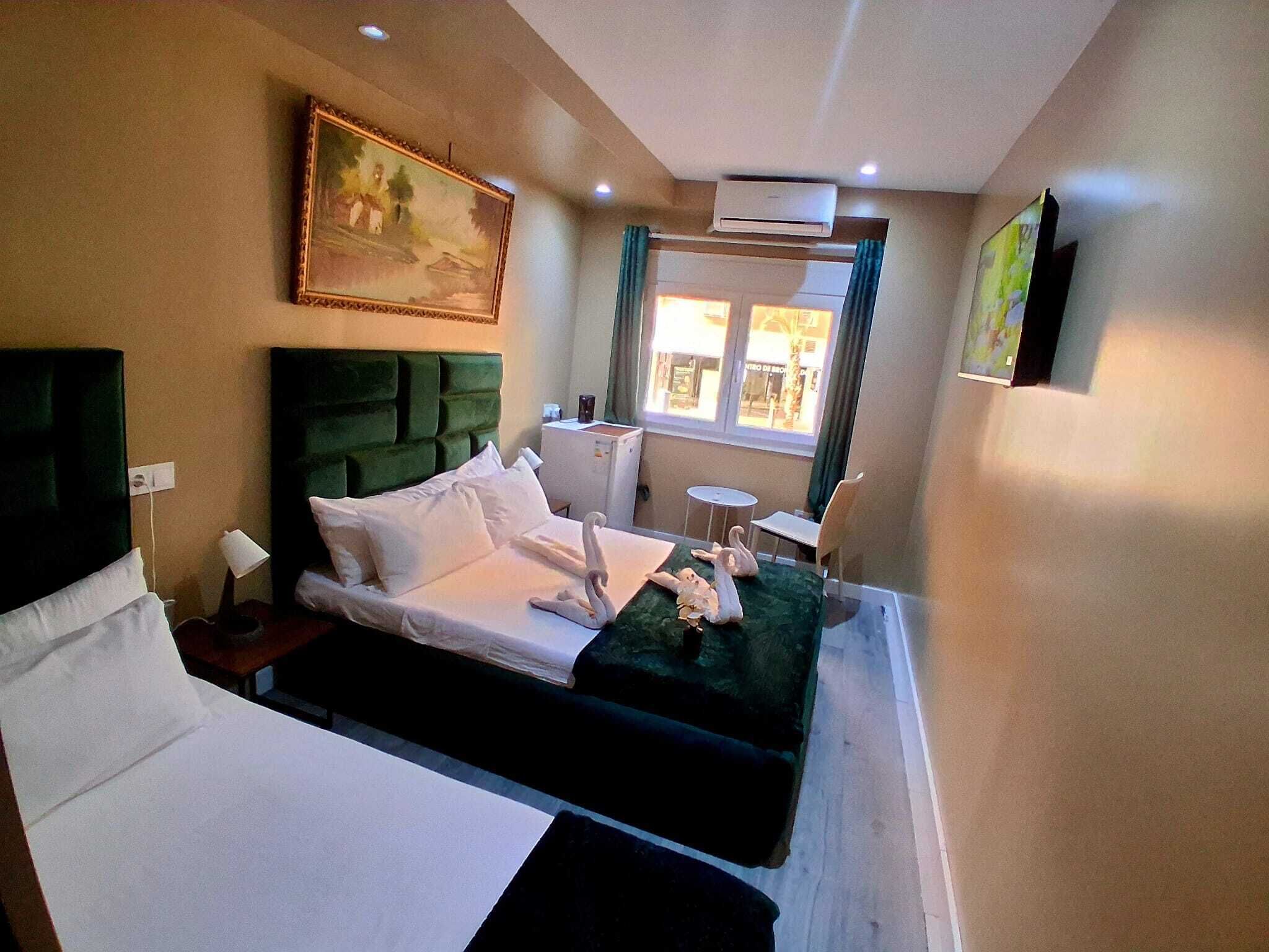 Habitación de hotel con cama, una mesita, una silla, un cuadro en la pared y una ventana con cortinas.