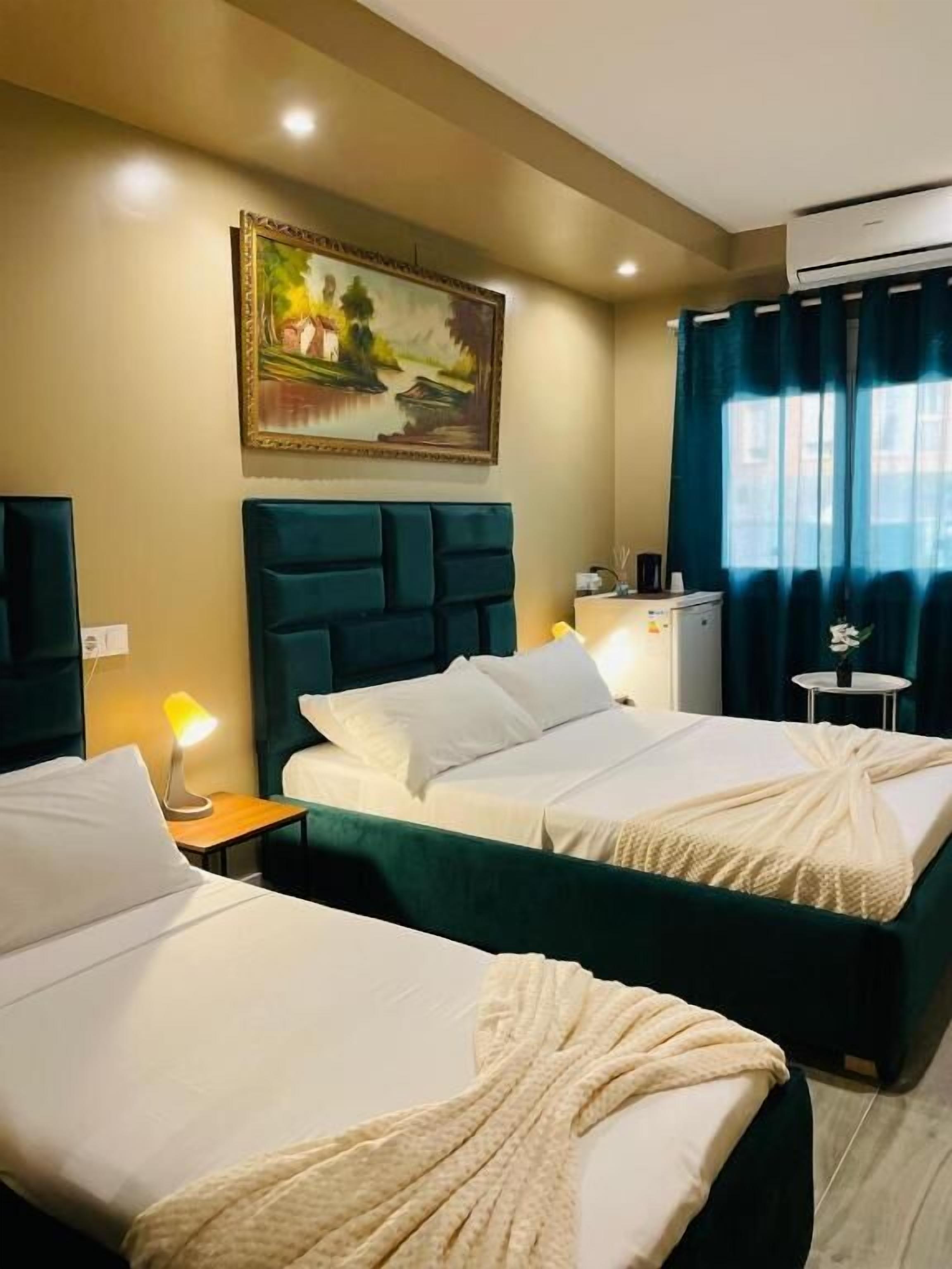 Habitación de hotel con dos camas, un cuadro en la pared, un equipo de aire acondicionado y una mesita de noche con lámpara.