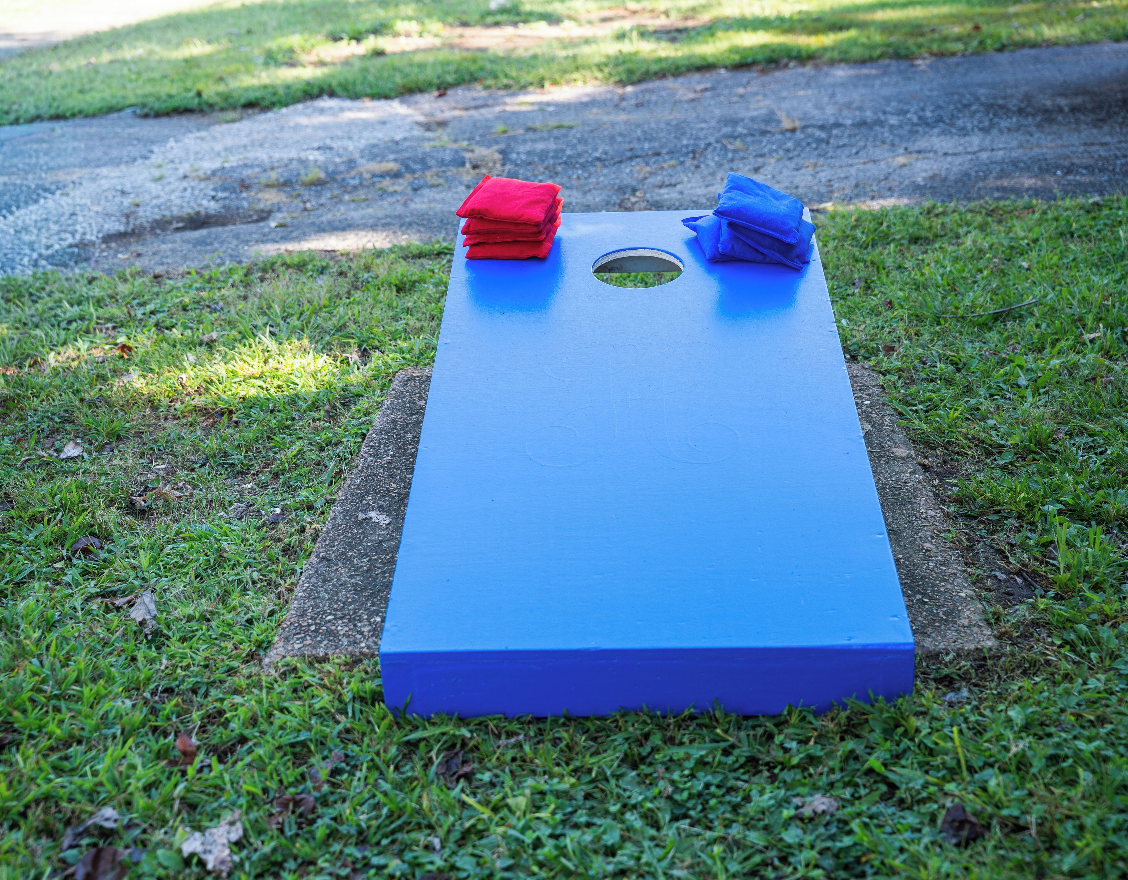 A blue board game with a hole in the center, placed on grass.