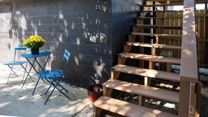 A wooden staircase leading up to a deck, a blue folding chair, a small table, and a potted plant. - The Clark: Where Superheroes Sleep! (Metropolis)