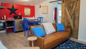 A living room with a brown leather sofa, blue chairs, a kitchen area with a red wall, and a wooden barn door. - The Clark: Where Superheroes Sleep! (Metropolis)