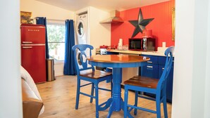 A compact kitchen with a red refrigerator, a washing machine, and a microwave. There is a blue table with two chairs and a star decoration on the wall. - The Clark: Where Superheroes Sleep! (Metropolis)