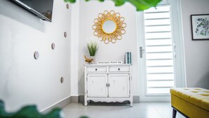 A room with a white cabinet, a yellow cushion, a mirror, and a framed artwork on the wall.
