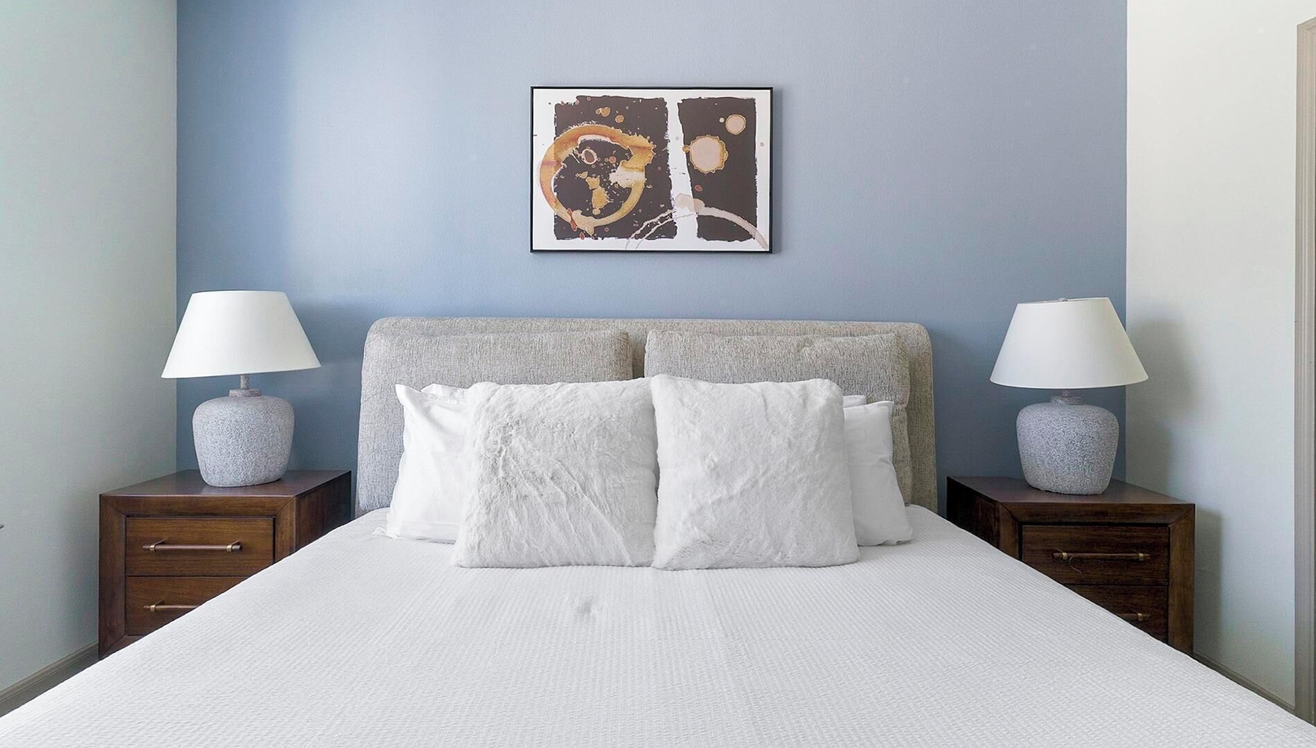 A neatly made bed with white linens, a grey headboard, and two bedside tables with lamps.
