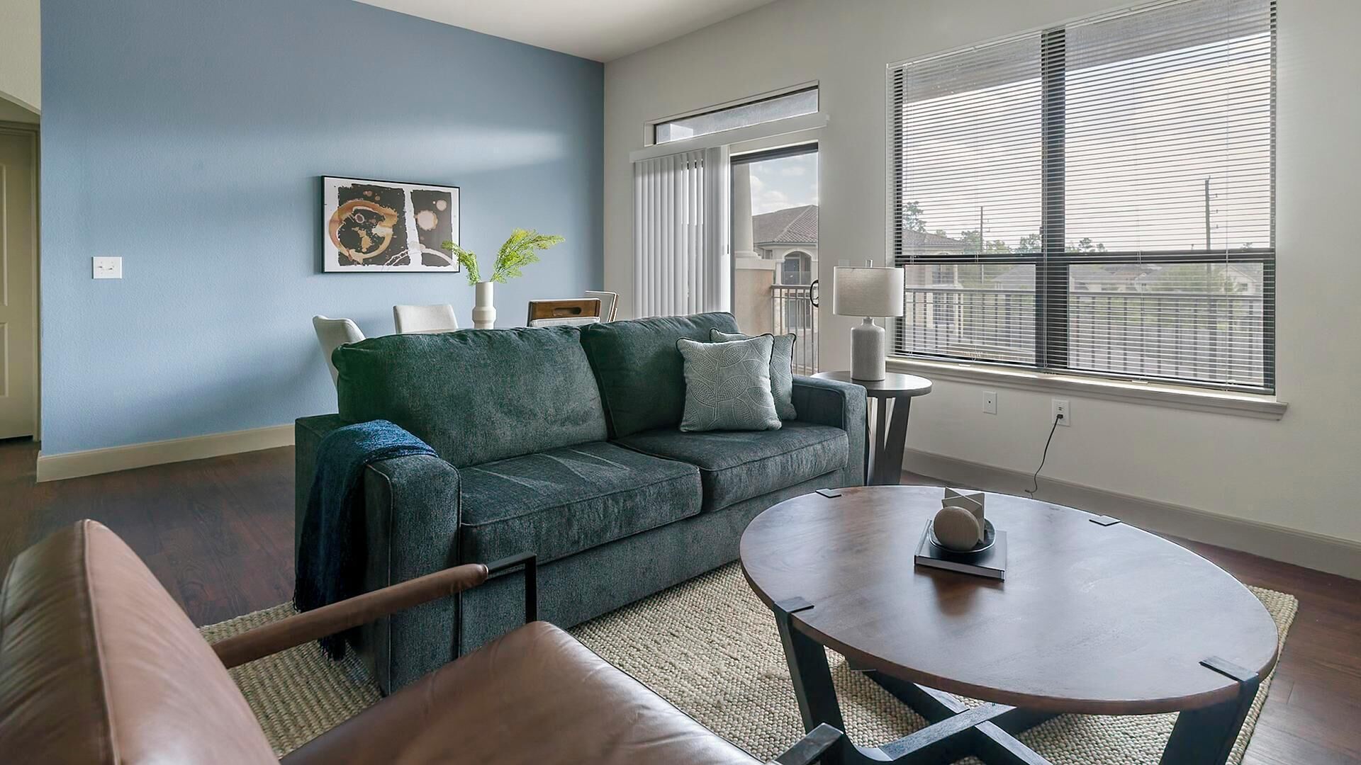 A living room with a green sofa, a round coffee table, and a view through large windows.
