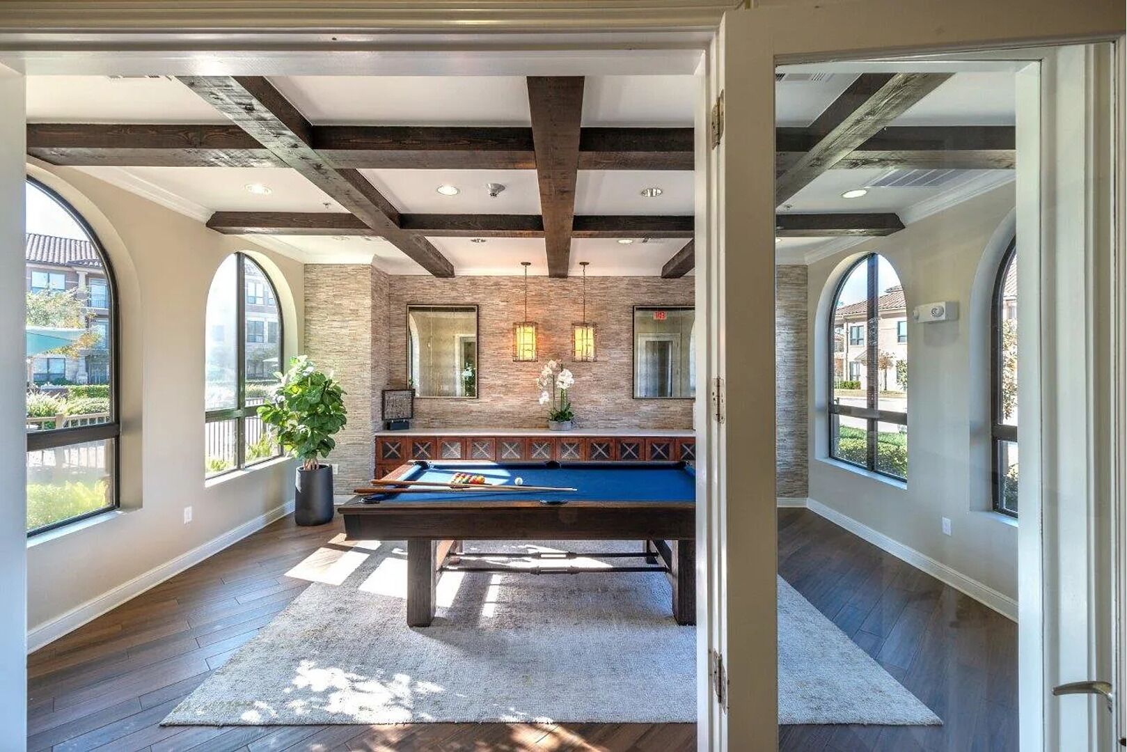 A pool room with a pool table, large windows, and a brick wall.