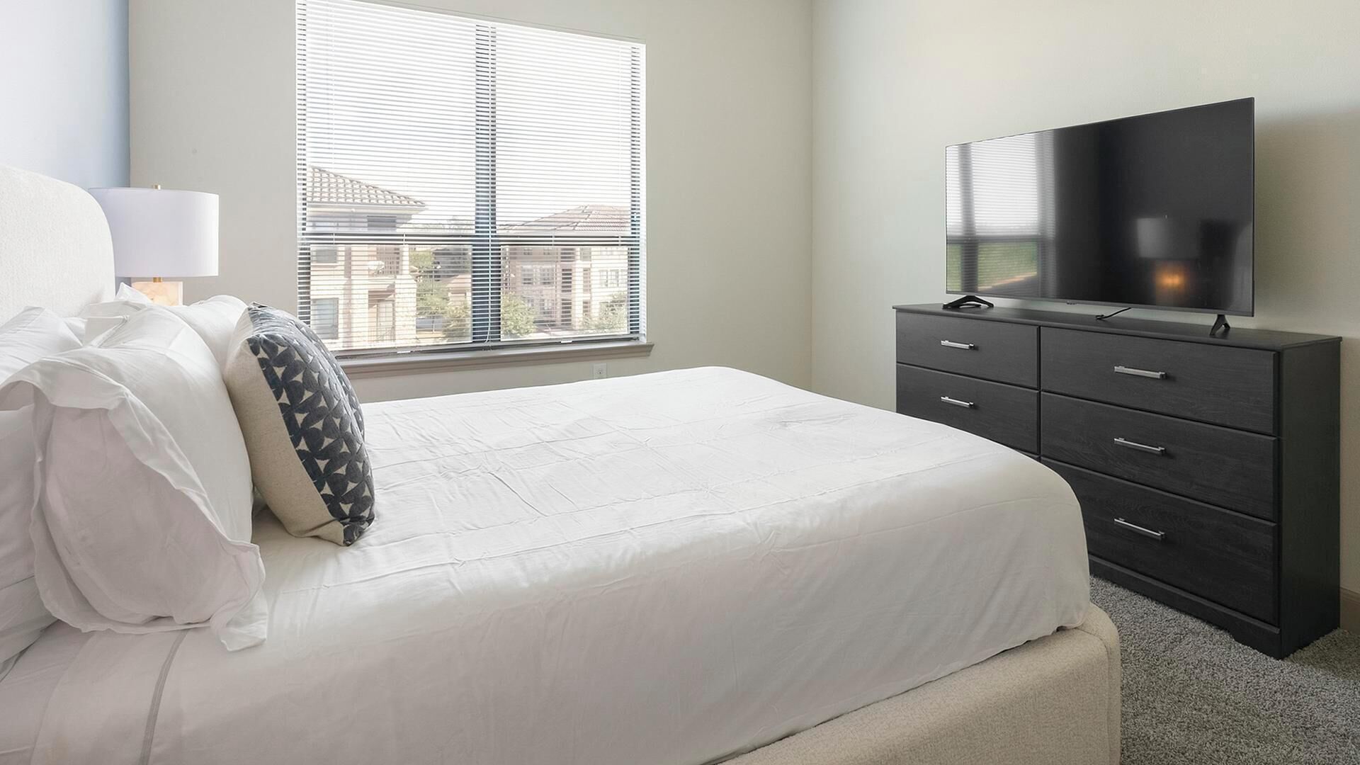 A bedroom with a bed, a dresser, a TV, and a window with blinds.