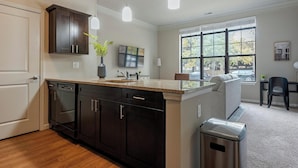 A modern kitchen with dark wood cabinets, a granite countertop, and a stainless steel trash can.