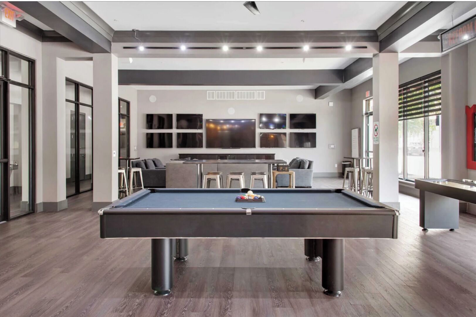 Mesa de bilhar moderna em ambiente interno, com acessórios de bilhar, área de bar e espaço de estar com sofá e cadeiras.