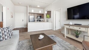 Una sala moderna con un sofá, una mesa de centro, un televisor y una zona de cocina con armarios y un refrigerador.