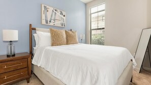 Quarto com cama, mesa de cabeceira, luminária, pintura e janela com persianas.