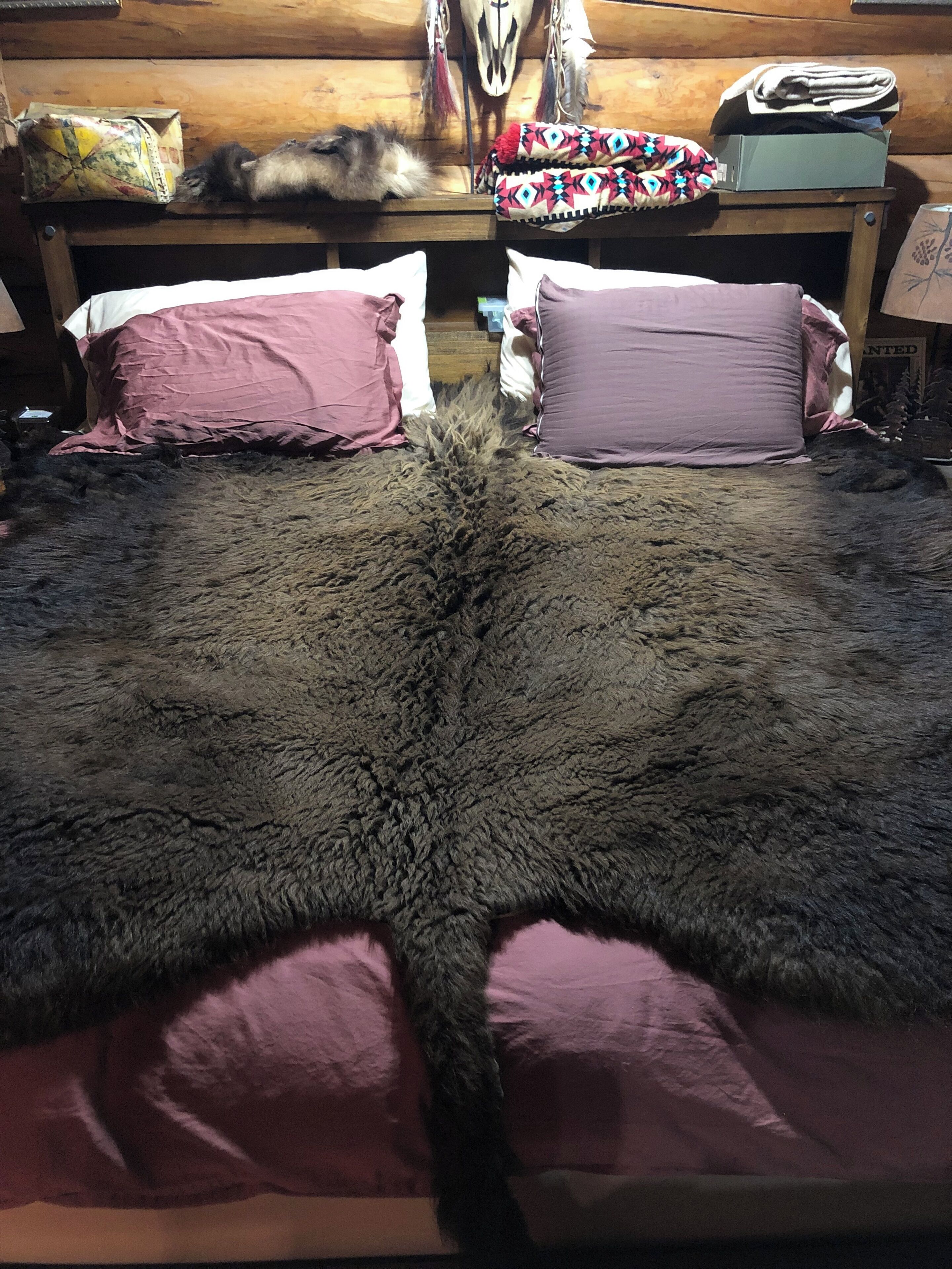 Una habitación con un tapete de piel grande, dos almohadas rosas, un cabecero de madera y una mesita con una caja y una almohada estampada.
