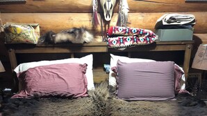 Une pièce avec une grande moquette en fourrure, deux coussins roses, une tête de lit en bois et une petite table sur laquelle se trouvent une boîte et un coussin à motifs.