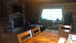 L’intérieur d’un chalet chaleureux, avec une cheminée en pierre, des meubles en bois et une grande fenêtre.