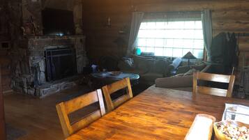 Interior acogedor de una cabaña con chimenea de piedra, mobiliario de madera y un ventanal grande.