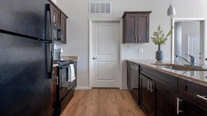 A modern kitchen with dark cabinetry, a stainless steel refrigerator, a microwave, and a sink with a vase of flowers. - Landing | Stylish 1BD, Gym, Pool (St. Louis)