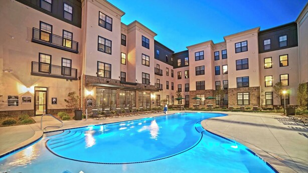 A swimming pool with lounge chairs, a bar area, and a building with multiple balconies. - Landing | Stylish 1BD, Gym, Pool (St. Louis)