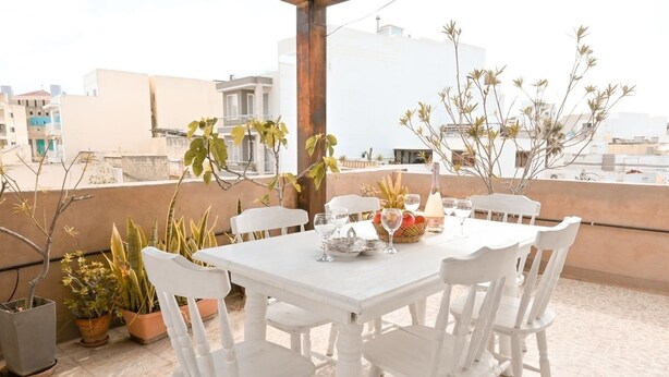 A white table and chairs set on a rooftop terrace with potted plants and a view of buildings. - 7 MEDITERRANEA VILLA (St. Paul's Bay)