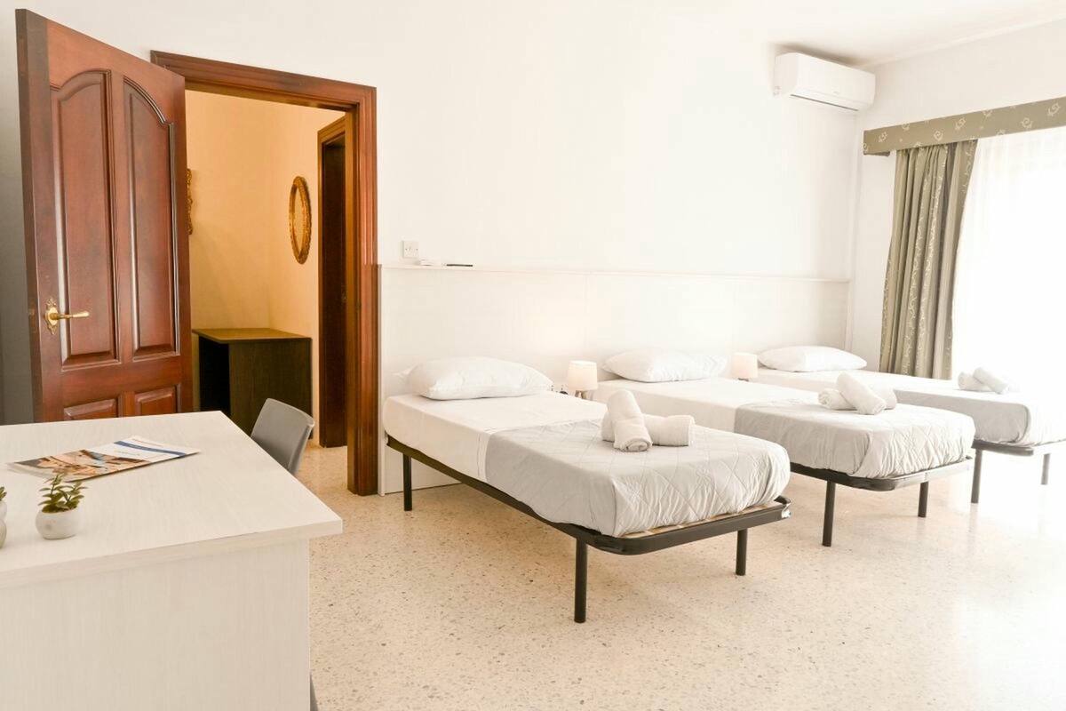 Een hotelkamer met een bureau, twee bedden, een deur en een airconditioning.