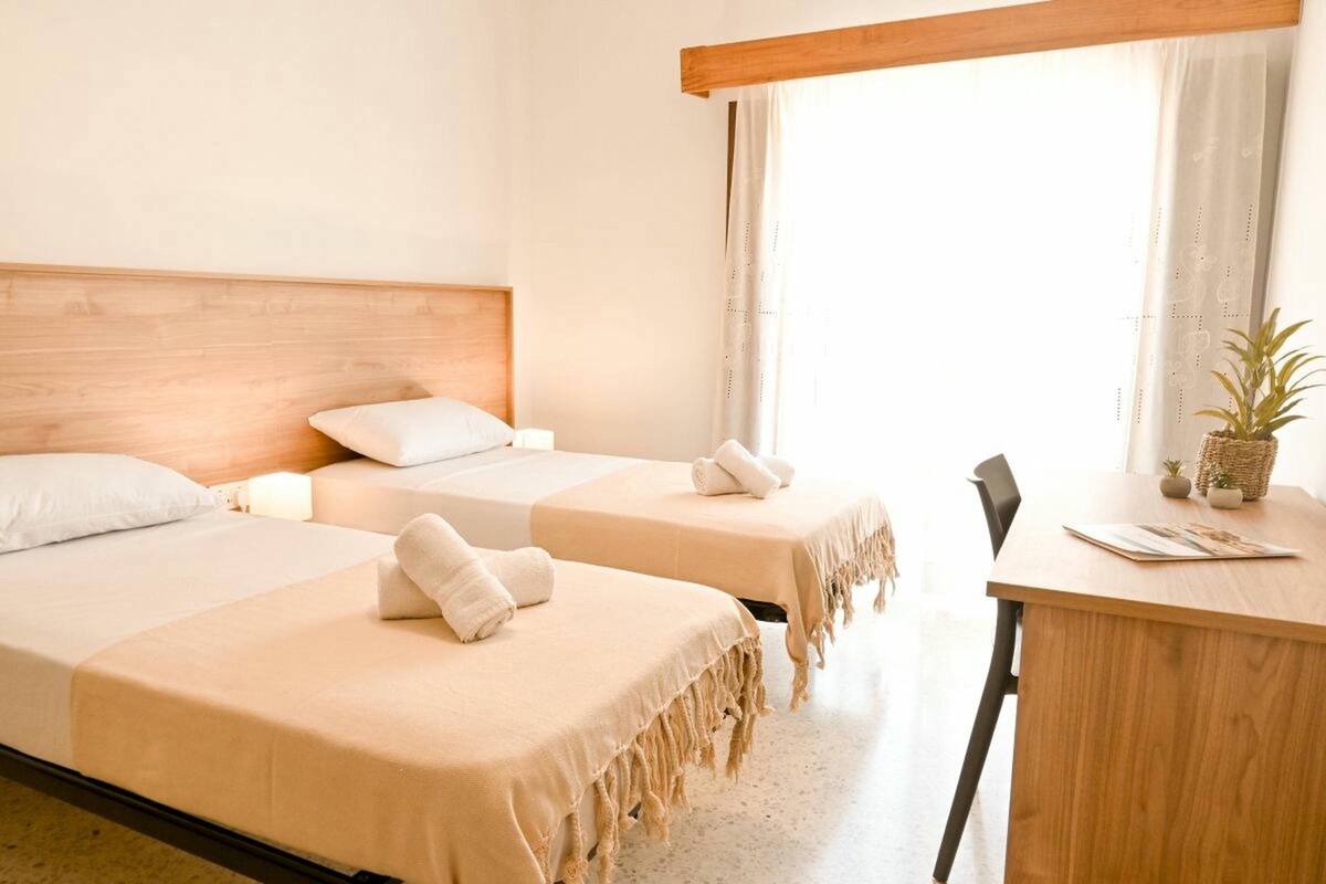 Een hotelkamer met twee bedden, een houten hoofdeinde, een bureau en een raam met gordijnen.